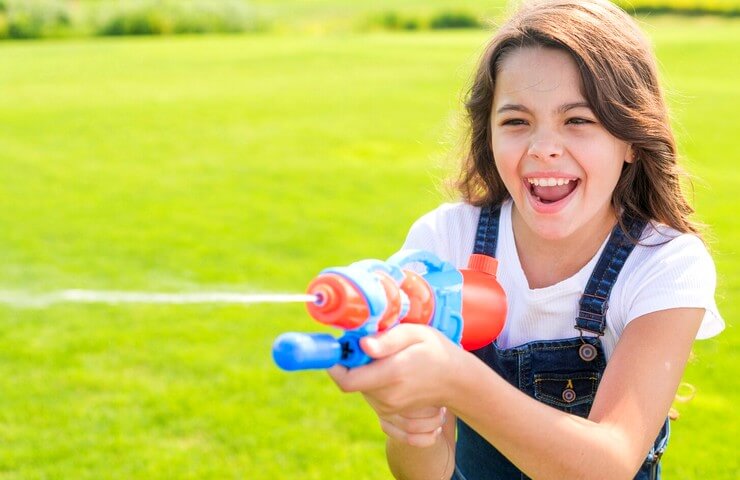 Fille souriante jouant avec un pistolet à eau